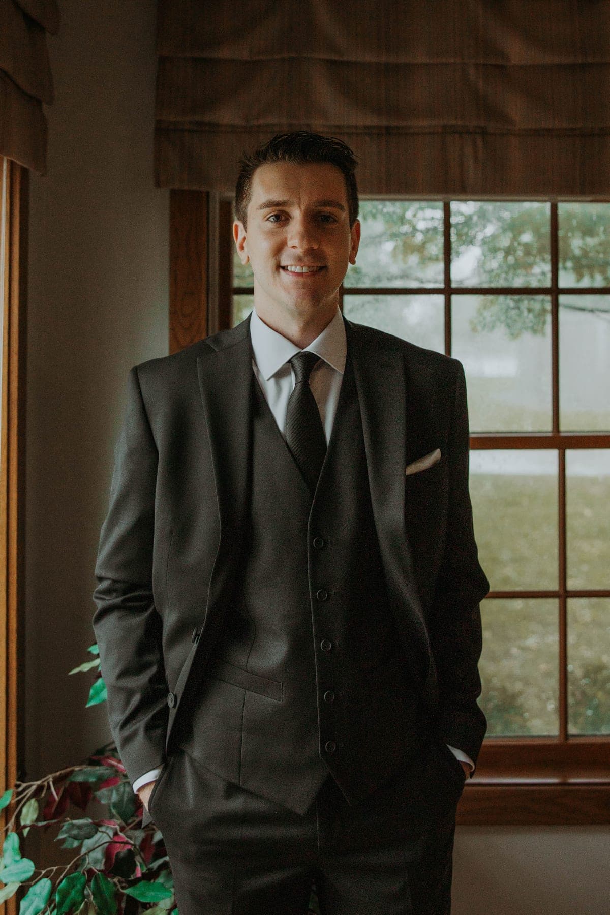 Connor Hagans, standing by a window in a dark three-piece suit, smiling